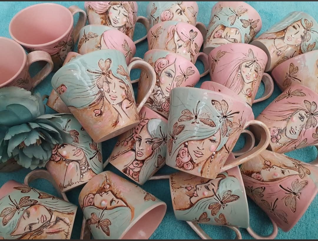 Suur hulk käsitööna valminud keraamilisi tasse kollektsioonist Kiilitar, mis on tihedalt üksteise kõrvale laotud rohekassinisel kangal. Tassidel vahelduvad pastelne roosa ja piparmündiroheline glasuur. Igal tassil on voolitud ja maalitud naisenägu, keda ümbritsevad detailsed kiilid. Pildi vasakus servas on kaunistuseks suur sinakasroheline tekstiillill.